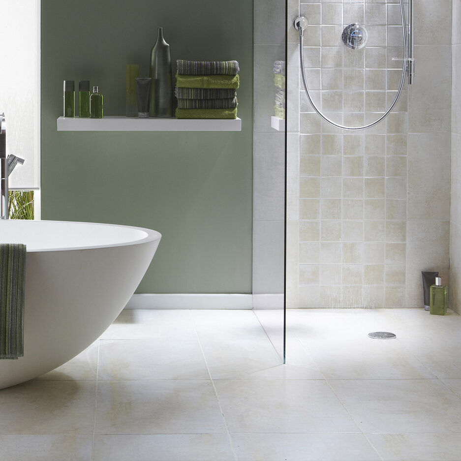 The interior of a simple, modern bathroom in a cool, green tone. There is a bath, shower, a bath towel . There are light grey tiles in the shower with running water
